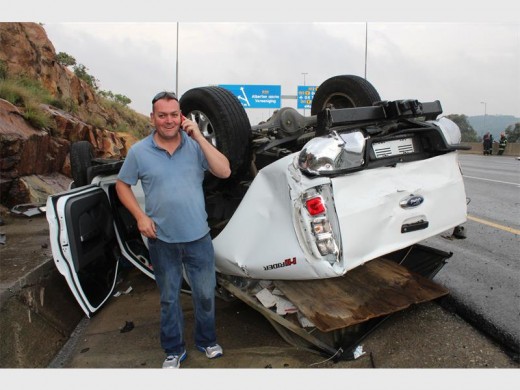 Shocked but grateful motorist, David McCullough, by the wreckage of his car and letting family members know he’s fine. Picture: Comaro Chronicle